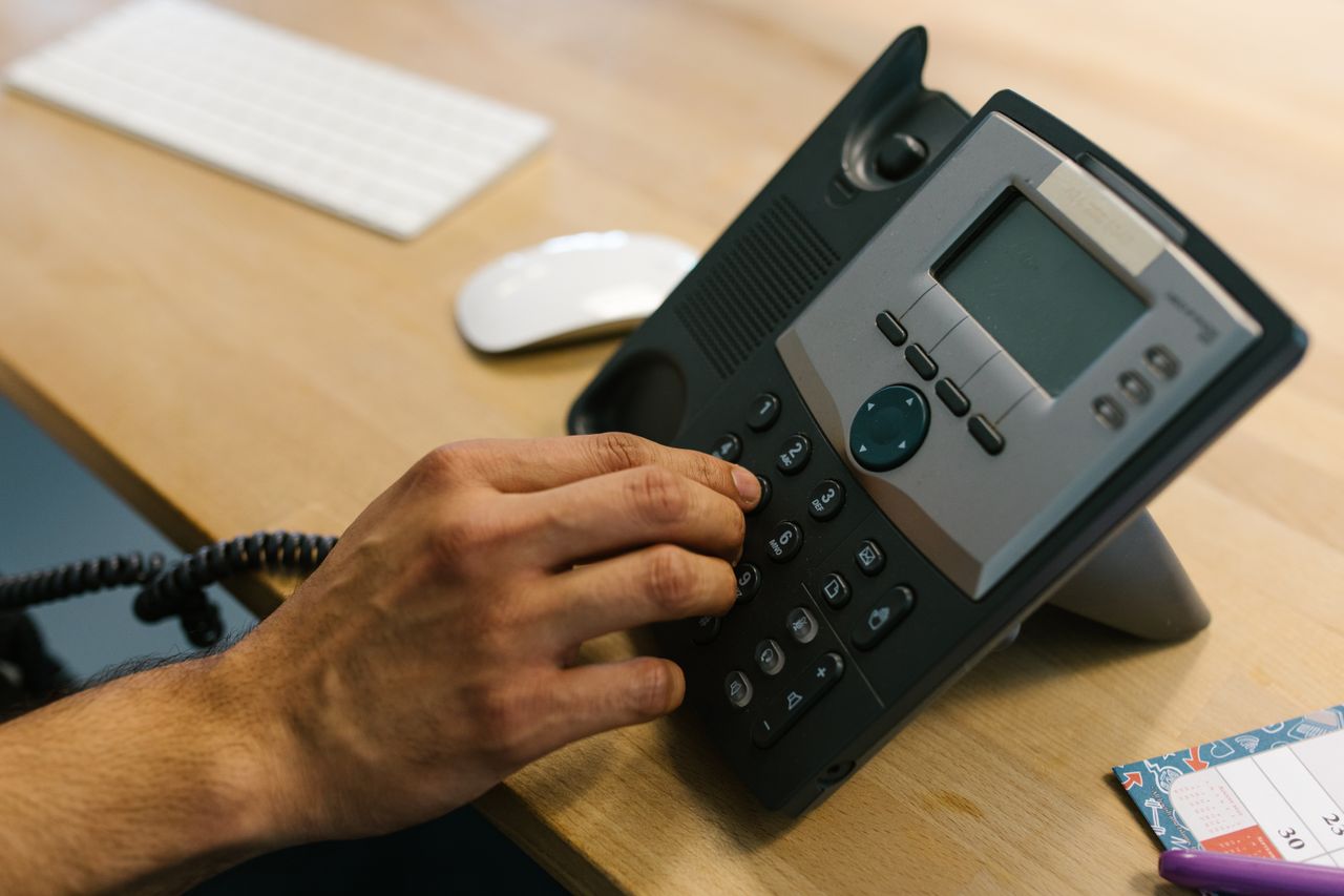 Crafting Captivating Headlines: Your awesome post title goes here A hand dialing a phone on a wooden desk. Office environment with keyboard and planner.