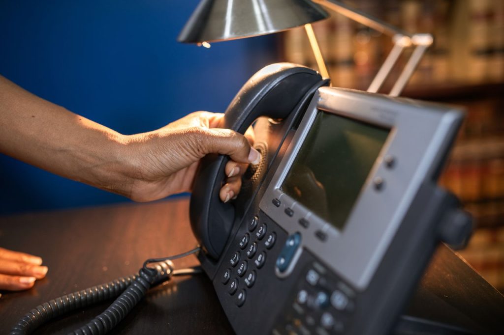 A close-up image of a hand picking up a handset from an office telephone, emphasizing communication device usage.
